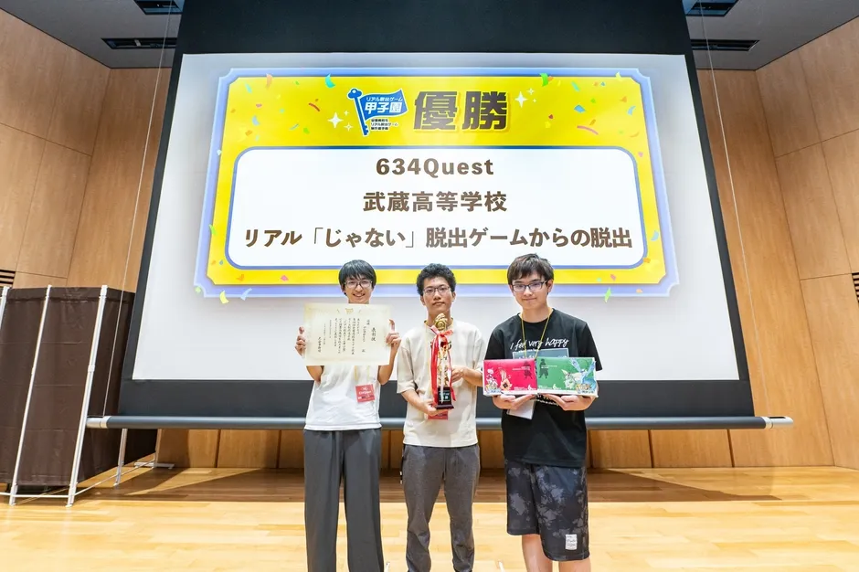 プレゼンテーションの前に立ってトロフィーと賞状を持っている3人の男性の画像。