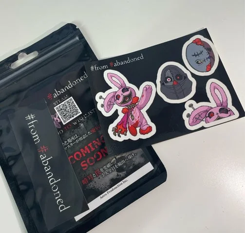 ピンクのウサギとキラーのキャラクターが描かれたステッカーシートと、黒いジップロック袋に入ったグッズ
